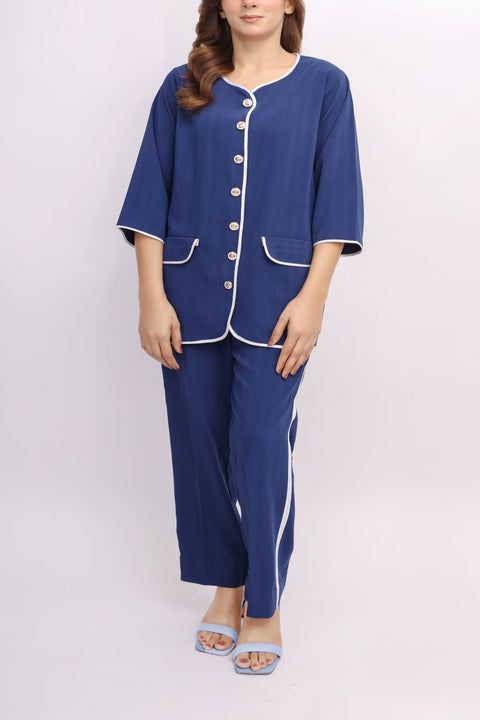 Woman wearing a blue pajama set with white trim on a light pink background — alternate view