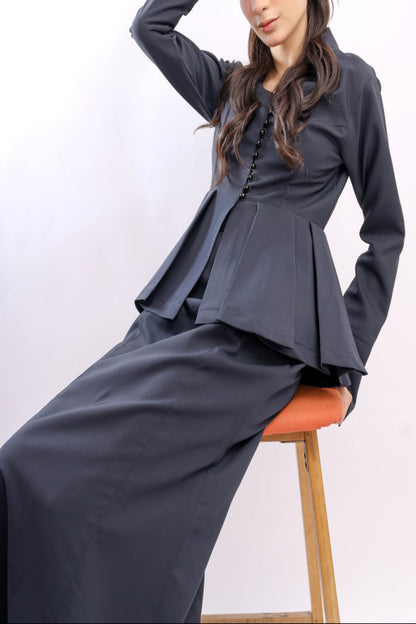Woman wearing a dark gray outfit sitting on an orange stool against a white background
