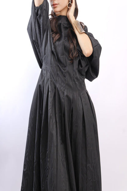 Person wearing a black dress with a subtle pattern on a light purple background